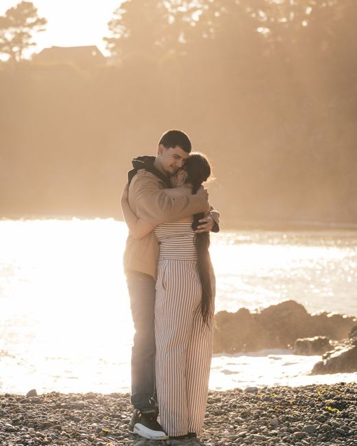 Backlit couple embracing by the water