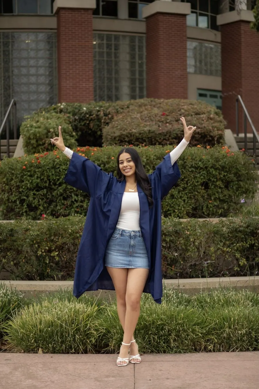 Graduate in her gown with both arms raised in celebration