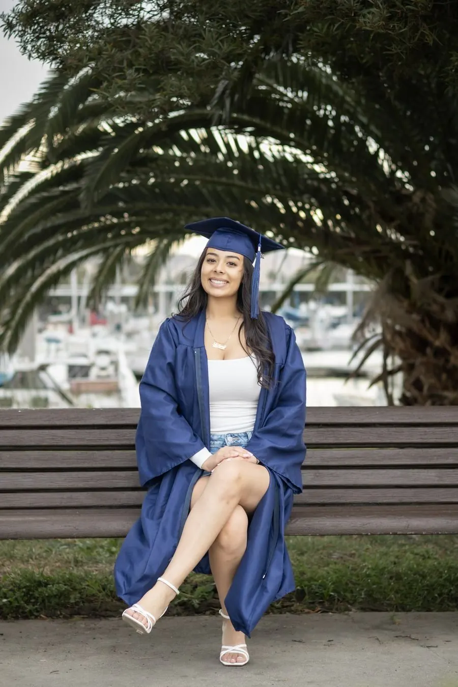 Graduate in cap and gown seated on a bench under a palm tree