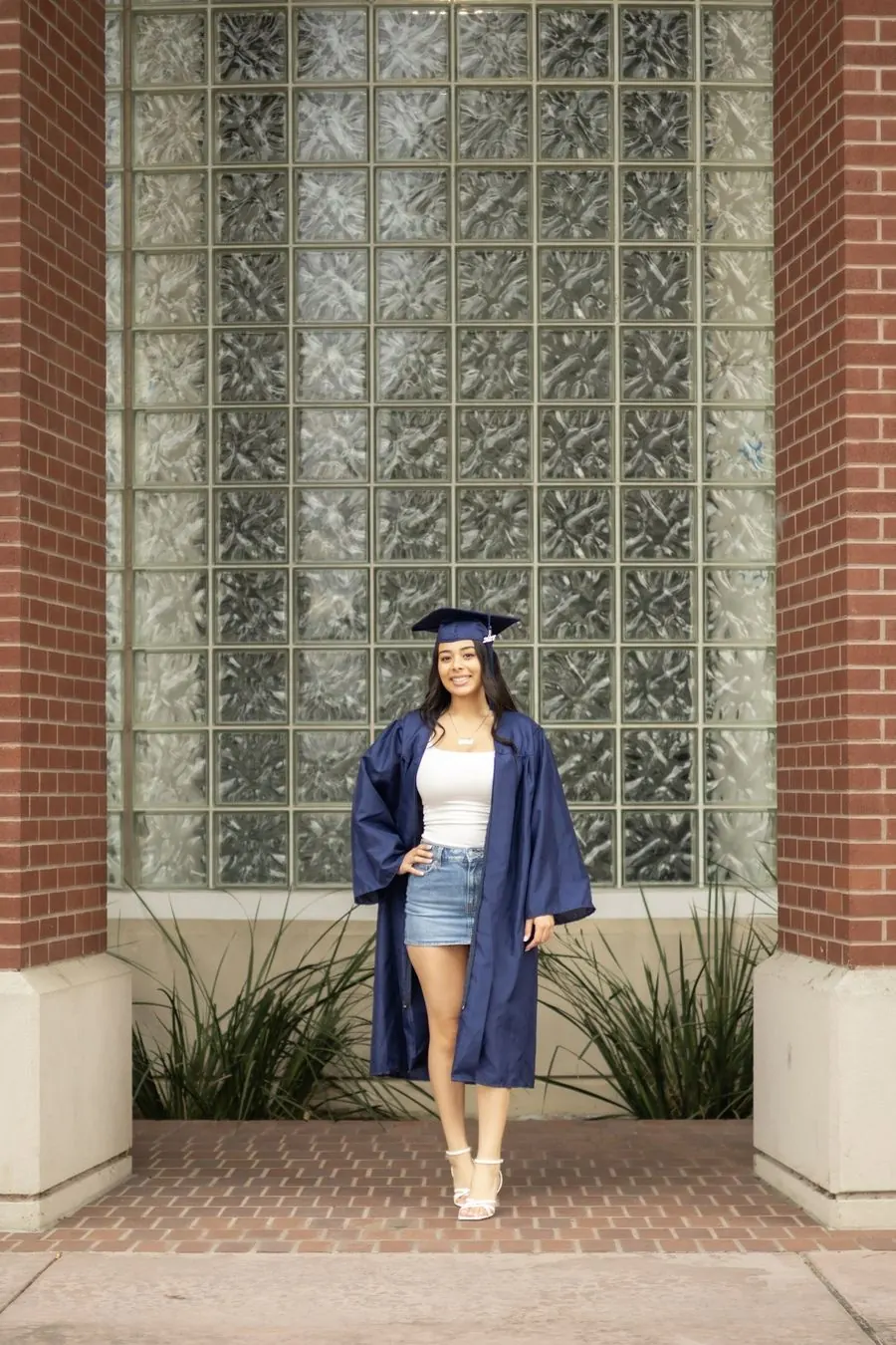 Graduate in cap and gown standing in front of a glass block window