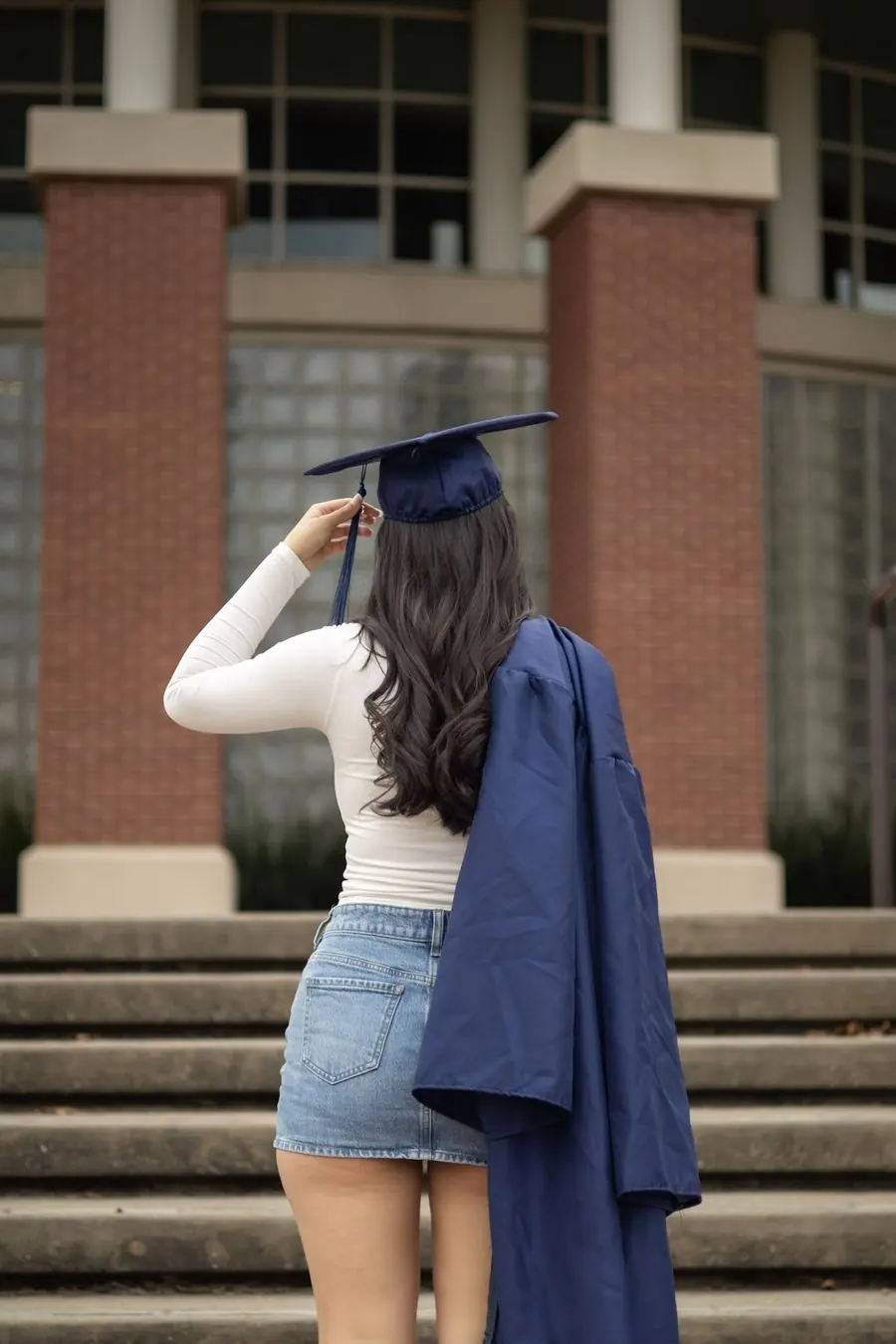 Graduate seen from behind adjusting her cap tassel in front of brick columns