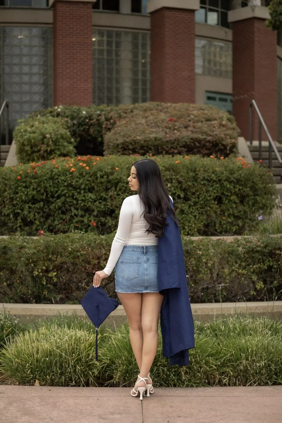 Graduate glancing over her shoulder, holding her cap, gown over her shoulder